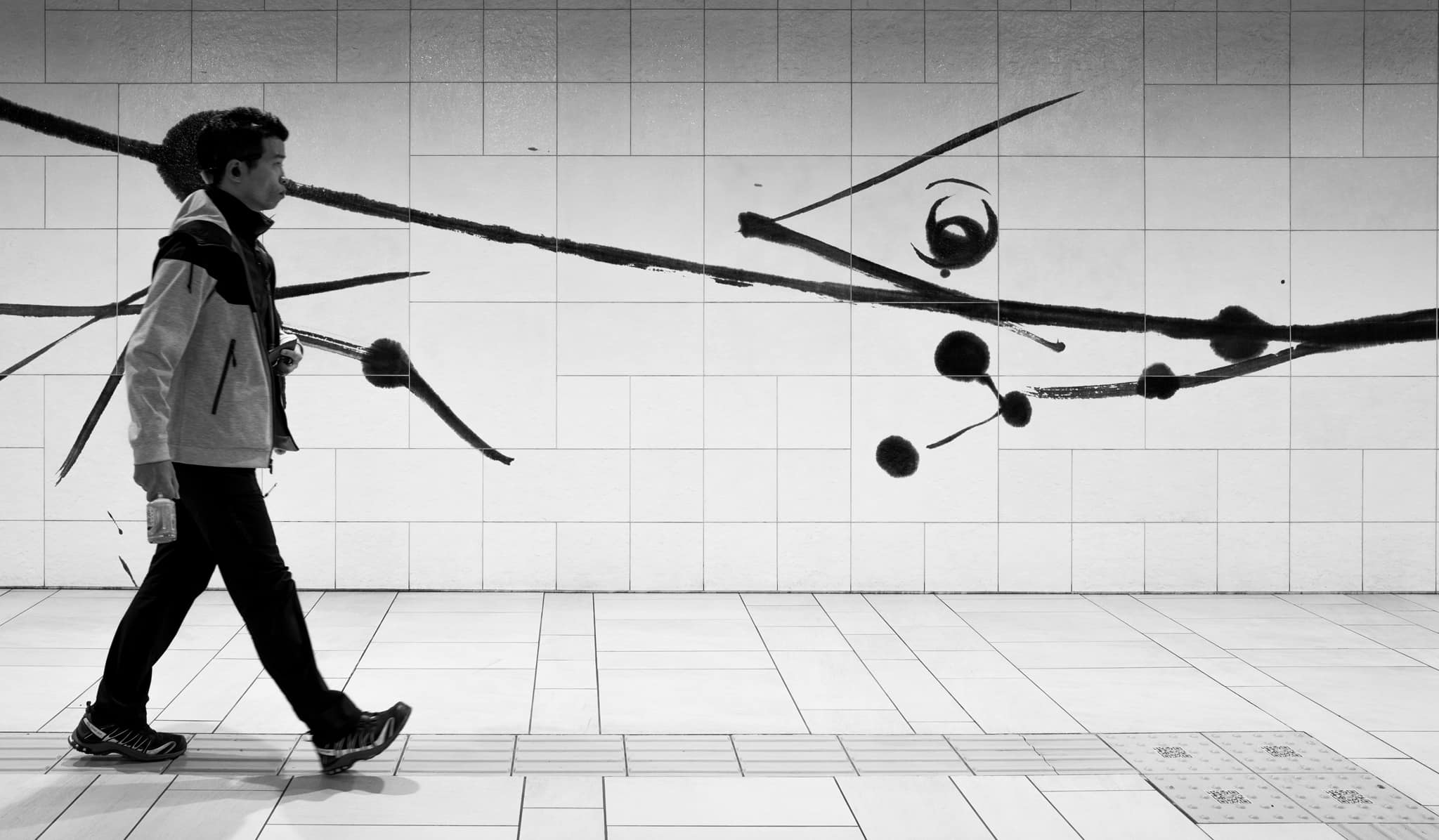 Person walking in a tiled hallway with abstract black and white art on the wall.