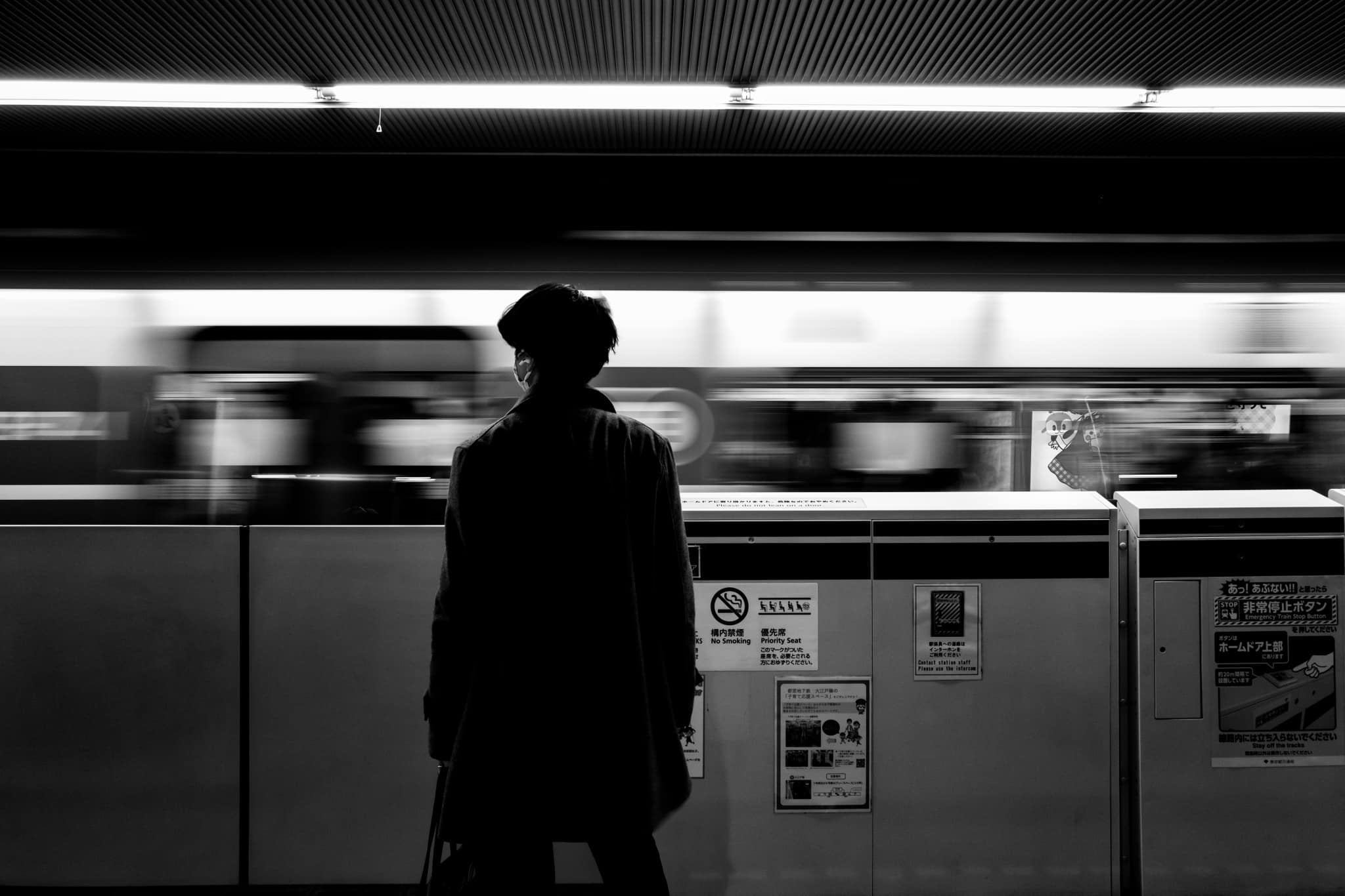 Person standing in a Tokyo subway station with a blurred train in the background