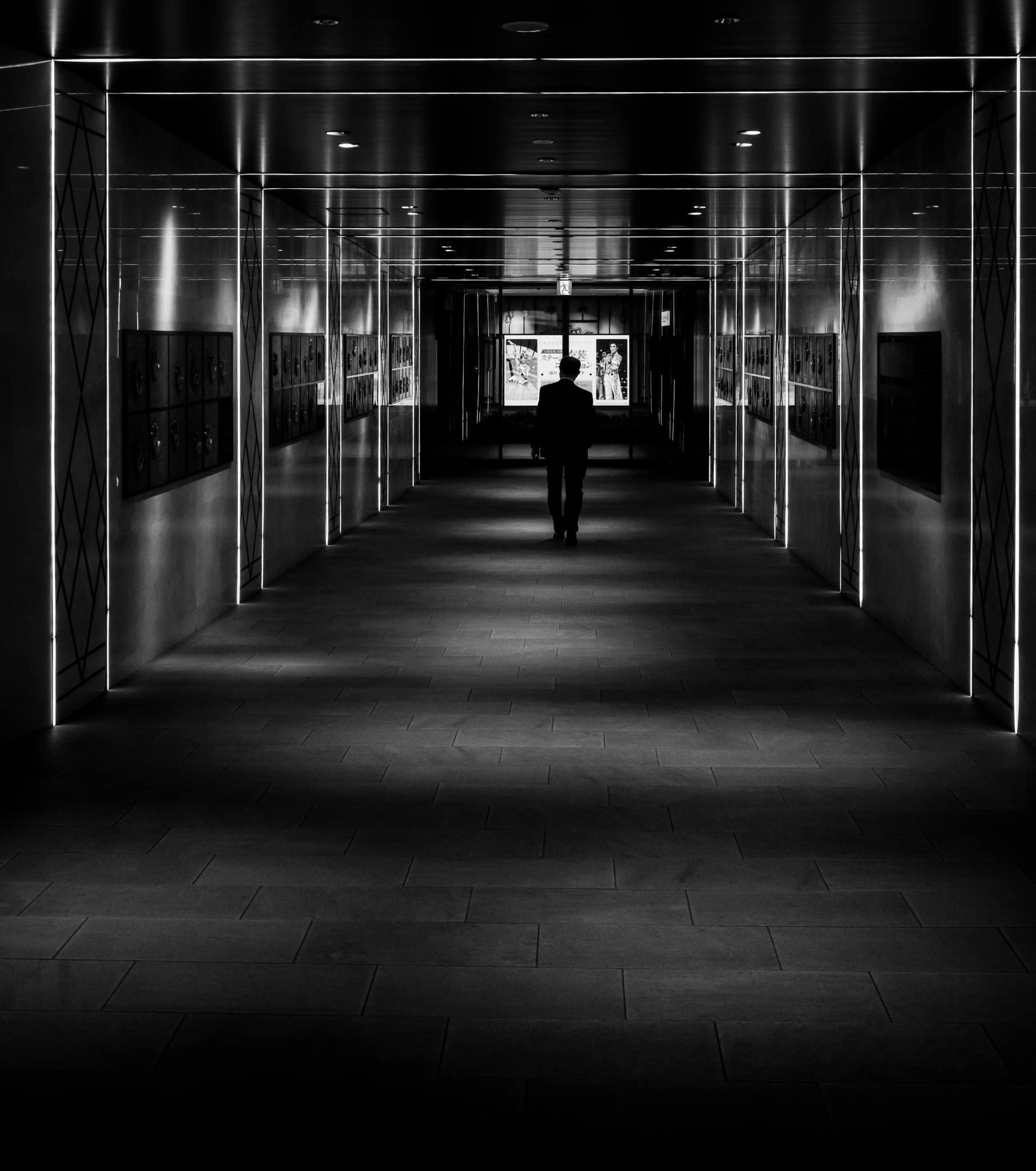 Silhouette of a person walking down a long, dark hallway with reflective walls.