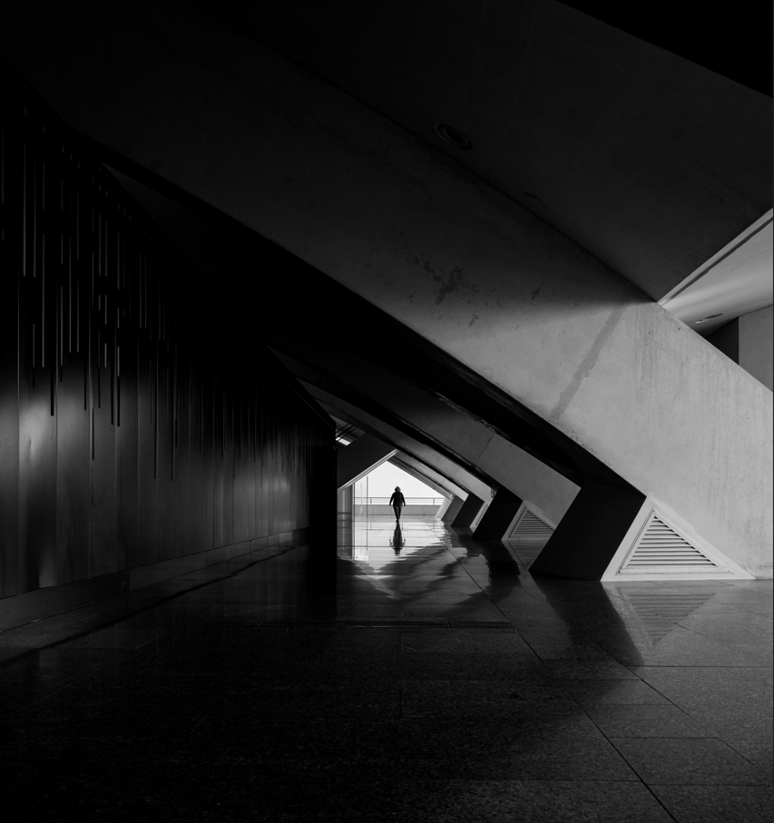 Person standing in a dark architectural hallway with light at the end