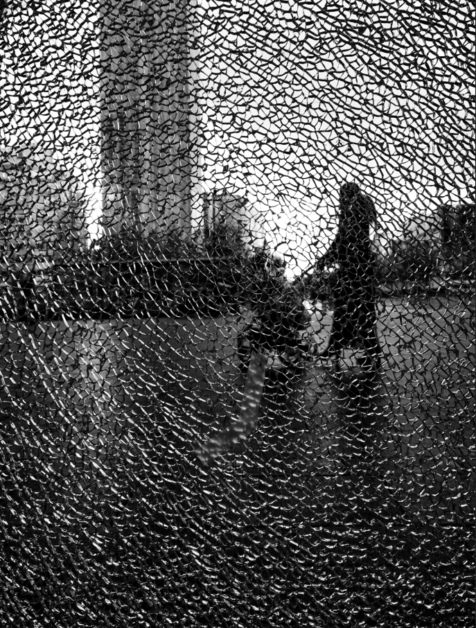 black and white photo of woman pushing pram through the view of shattered glass 
