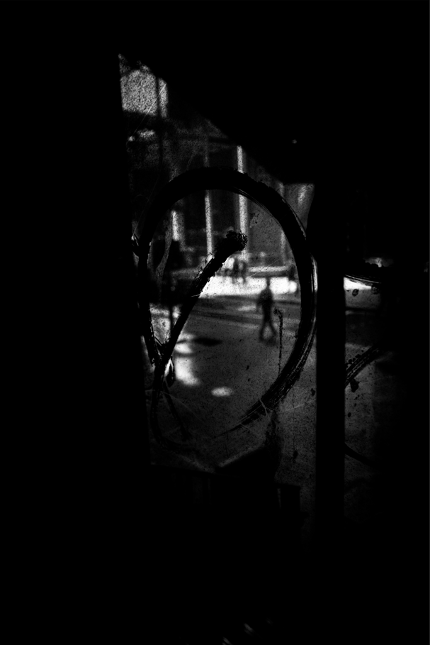 black and white photo of a man walking down the street as seen through a window 