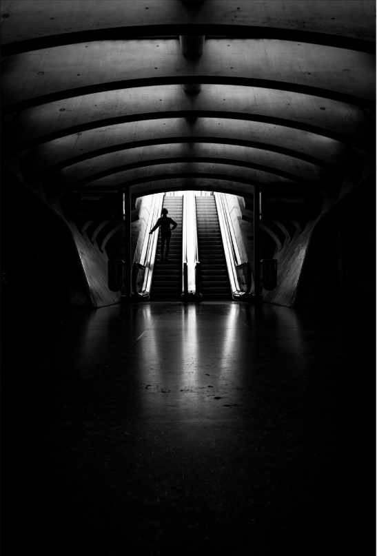 Person ascending an escalator in a dark tunnel in train station