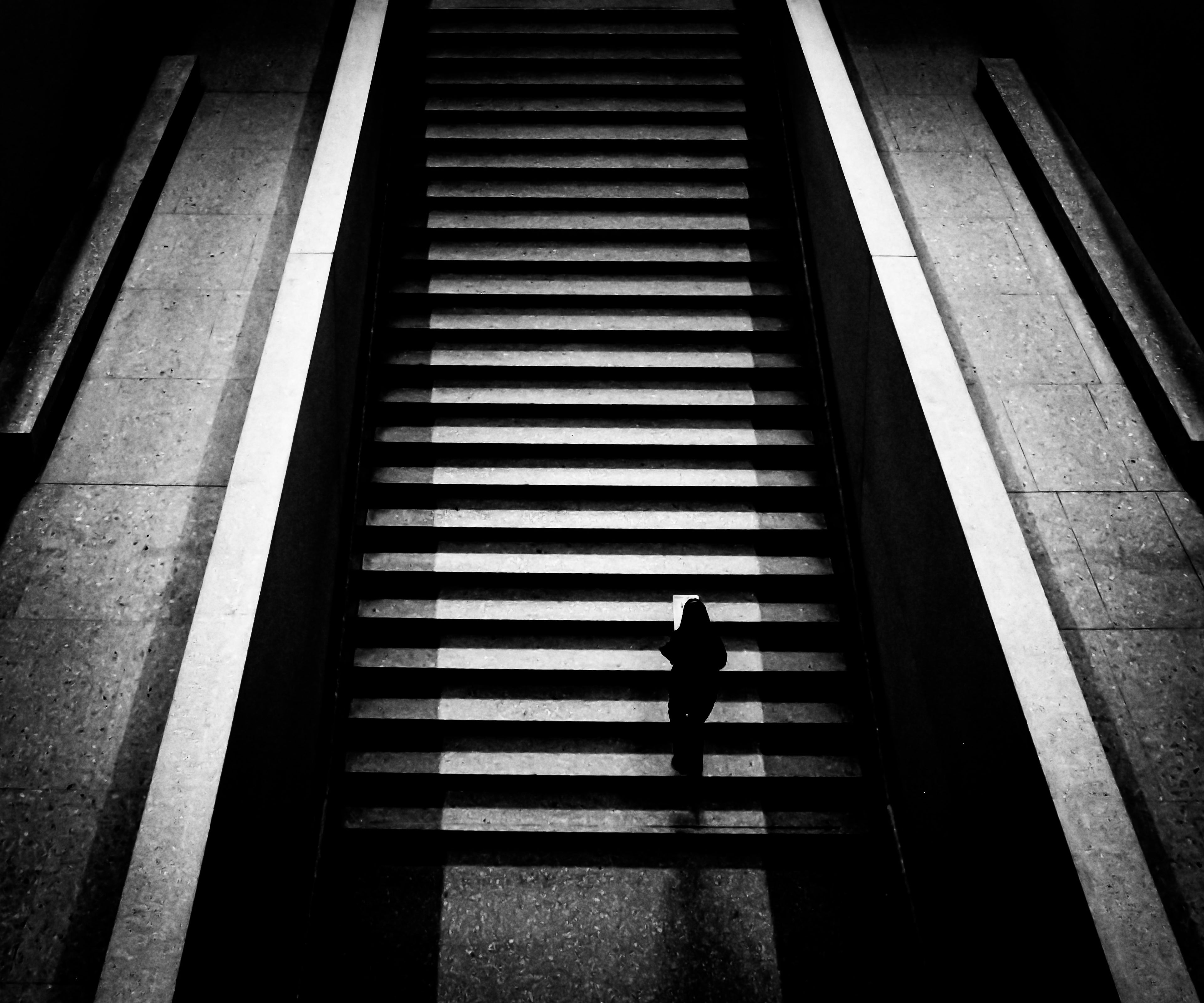 Black and white photo of a person standing on a set of stairs with a long shadow